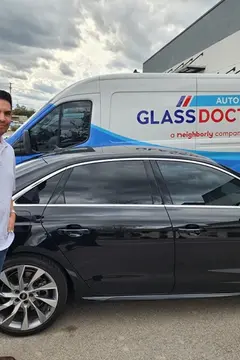 A happy customer poses in front of his black car with a Glass Doctor Auto of Cedar Park truck in the background.