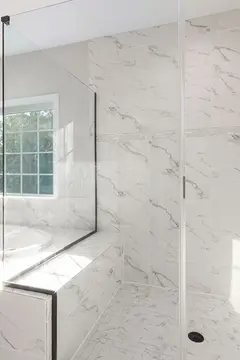 A marble-tiled shower with clear frameless glass enclosure next to a raised tub.