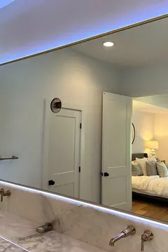 A bathroom mirror over a double-sink vanity with a gold frame, back-lighting, and three round cutouts for light fixtures by Glass Doctor of Nashville.