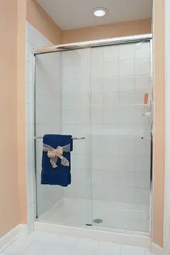 A white tiled walk-in shower with a sliding glass door and chrome top frame.