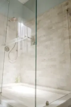 A bathroom with gray walls and a shower with beige tiles and a frameless enclosure made of clear glass panels.