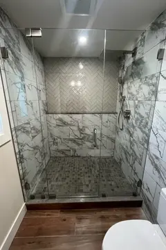 A frameless glass shower door on a marble tiled shower in a full bathroom remodel project by Glass Doctor of Tampa Bay.
