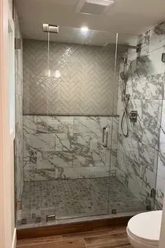 A custom frameless glass shower door installed on a shower with marble tiles as part of a bathroom remodel by Glass Doctor of Pinellas County.