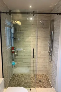 A sliding glass shower door with black hardware installed on a walk-in shower by Glass Doctor of York Region.