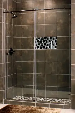 A shower with two-panel sliding frameless glass doors and dark brown tiles.