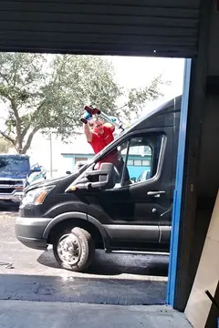 An auto glass specialist from Glass Doctor of Tampa Bay installing a new windshield on a black Sprinter van. 