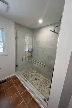 A shower with grey tiles and a frameless glass enclosure and swinging door by Glass Doctor of Muskoka.