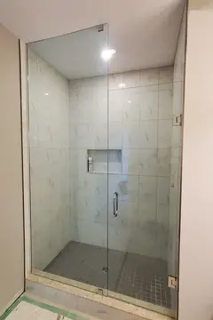 A shower with a custom straight across glass enclosure featuring a floor-to-ceiling panel and a swinging glass door from Glass Doctor of Newmarket.
