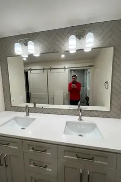 A mirror mounted on a gray tiled wall over a double-sink vanity on a bathroom remodel project by Glass Doctor of Tampa Bay.
