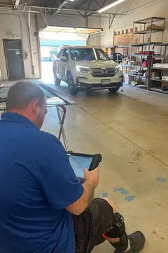 A white SUV in the work bay and a Glass Doctor Auto of Castle Rock service professional in the foreground looking at a tablet.