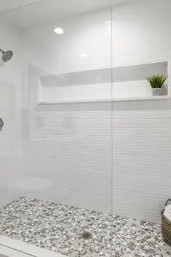 A walk-in shower with white tiles and a frameless clear glass splash panel.