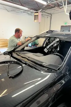 Two Glass Doctor Auto of Castle Rock service professionals working on a windshield replacement on a dark gray vehicle.