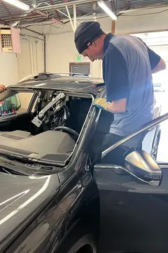 A Glass Doctor Auto of Castle Rock service professional standing in the door of a vehicle and working on a windshield replacement.