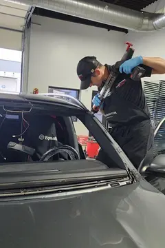 A skilled Glass Doctor Auto of Cedar Park uses an adhesive gun to apply adhesive to a gray car for a windshield replacement.