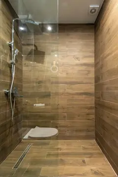 A shower with wood-grained tile and a clear glass splash panel.