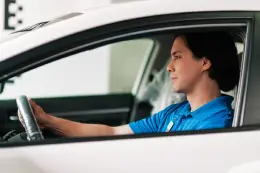 A person wearing a blue shirt sits in the driver's seat of a white car.
