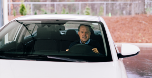 A man sitting inside of white car and pulling into a Glass Doctor service center.