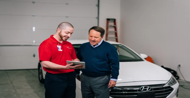 A man and a male Glass Doctor service professional reviewing a tablet with a white car behind them