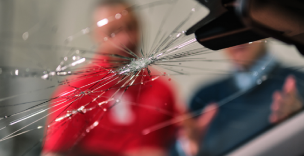 A man and male Glass Doctor service professional staring at a cracked windshield inside an auto facility.
