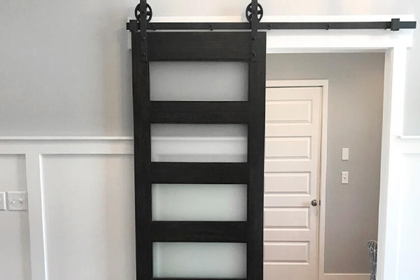 A black sliding door with glass panels, set in a well-lit room, showcasing a modern interior design.