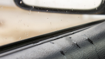 A close-up of a car window covered in raindrops, creating a blurred view of the outside.