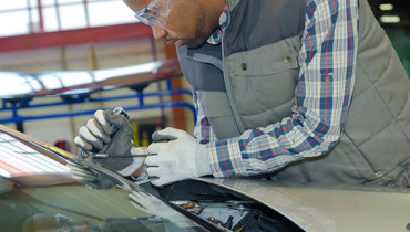 A man is focused on repairing a car in a garage, surrounded by tools and automotive parts.