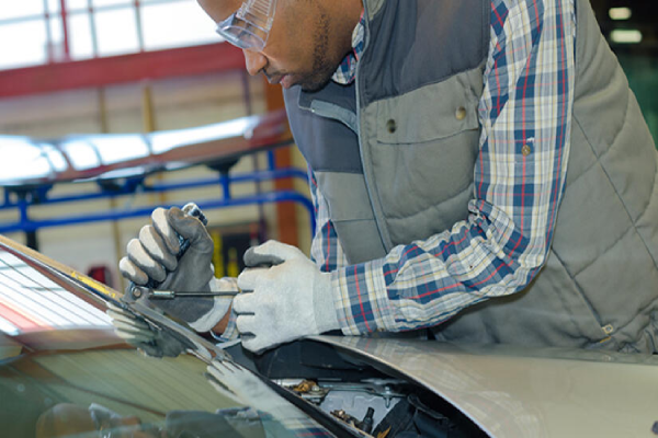 A man is focused on repairing a car in a garage, surrounded by tools and automotive parts.