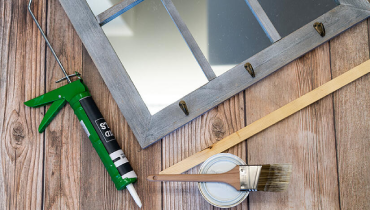 A mirror, paintbrush, and glue gun arranged on a wooden table, showcasing crafting tools for creative projects.