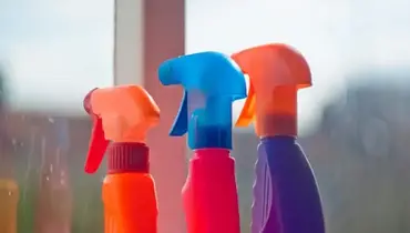 Three different glass cleaner bottles next to a window