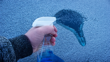 Man using liquid spray bottle to remove ice from car window.